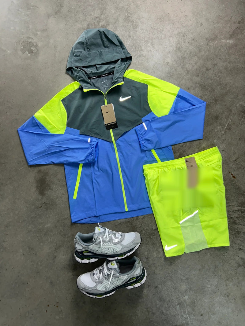 Ensemble running Nike 2 pièces bleu et volt : veste à capuche et short jaune fluo posés à plat avec une paire de baskets